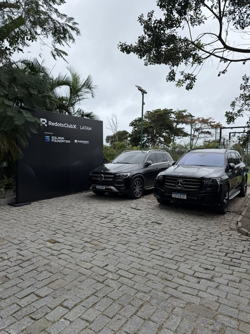 Two Mercedes-Benz SUVs parked on a cobblestone driveway next to a black sign reading 'RedotsClubX LATAM', 'SOLANA FOUNDATION', and 'Hyperliquid'.