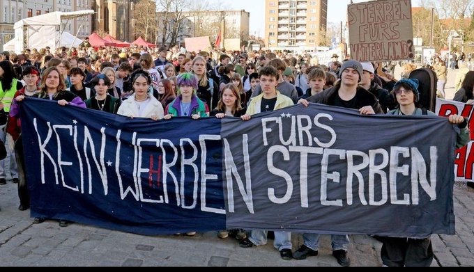 A crowd of young protesters holds a large dark banner reading 'KEIN WERBEN FÜRS STERBEN' (No Advertising for Dying), with another sign visible reading 'STERREN FÜRS VATERLAND' in the background.