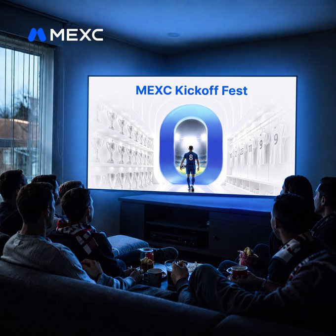 The image shows a group of people sitting together, watching a soccer game on television. They appear to be enjoying their time while munching snacks and drinks during the kick-off event organized by the Mexico Soccer Board (MEXC). The group is seated in front of a large screen TV placed above a wooden coffee table, which has various food items like bowls, cups, and sandwiches on it. Each person in the group seems to be engaged in watching the soccer match as they eat and socialize with one another during this event.