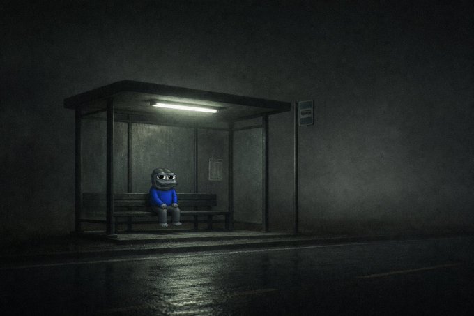 A small, wide-eyed cartoon character in a blue shirt sits alone on a bench inside a dimly lit bus stop at night.