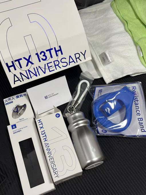 HTX 13th Anniversary merchandise is displayed, including a large box, a silver water bottle, a blue resistance band, and other branded items.