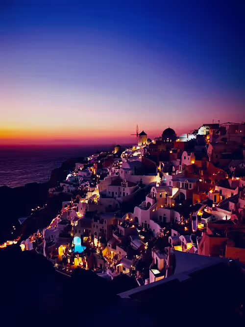 A scenic sunset view over Oia, Santorini, Greece, showing the white cliffside buildings and a windmill illuminated against a purple and orange sky.