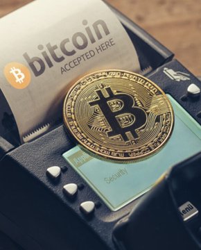 A physical Bitcoin token rests beside a receipt on a payment terminal displaying "bitcoin ACCEPTED HERE," symbolizing the early promise of crypto adoption in El Salvador. The image ties directly to the news that such bitcoin transactions at places like El Zonte's "Bitcoin Beach" have dwindled to nearly none, illustrating the gap between promotional imagery and real-world usage.