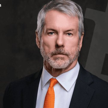 A professional portrait of a man with gray hair and a beard, wearing a dark suit, light blue shirt, and an orange tie against a dark background.