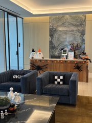A modern luxury living room featuring two gray armchairs, a marble-top coffee table, and a wooden sideboard against a blue marble accent wall.