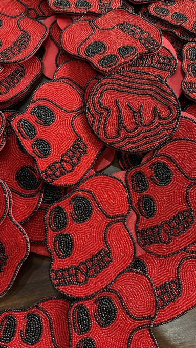 A close-up view of numerous handmade beaded skull patches in red and black, stacked on top of each other.