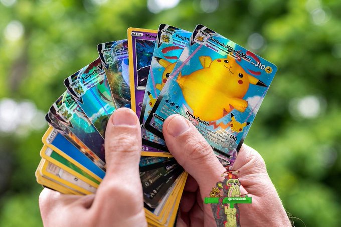 Hands fanning out a collection of Pokémon trading cards featuring Pikachu ("Dyna-Burten", 160 HP) and VMAX cards (310 HP) including Fiegelon and Flugdanel, with a "GeekAlarm" watermark.