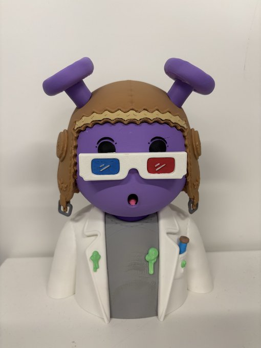 A 3D-printed figurine of a purple alien-like character with purple antennae, a brown aviator cap, 3D glasses, and a white lab coat with green slime details.