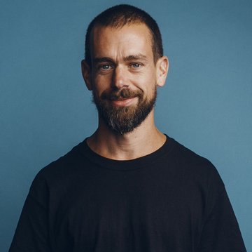 A portrait photograph of a smiling bearded man wearing a dark sweater against a blue background.