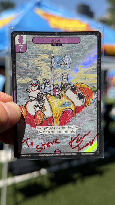 A hand holds up a signed promotional card titled 'Set Sail' (Action, cost 7), with handwritten text 'To Steve' at the bottom, against a blurred festival background.