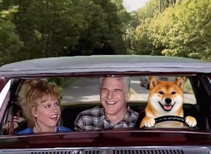 A humorous edited photo of a 1980s-style couple laughing in the front seat of a car, with a smiling Shiba Inu dog superimposed in the driver's seat holding the steering wheel.