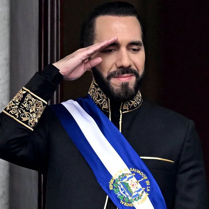 Nayib Bukay, President of El Salvador, wearing a formal black military-style jacket and a blue and white presidential sash, saluting with his right hand.