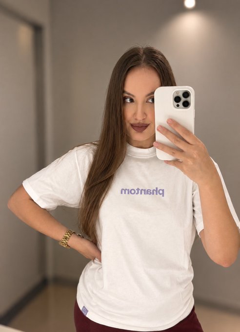 A woman takes a mirror selfie wearing a white t-shirt featuring the text 'meistern'