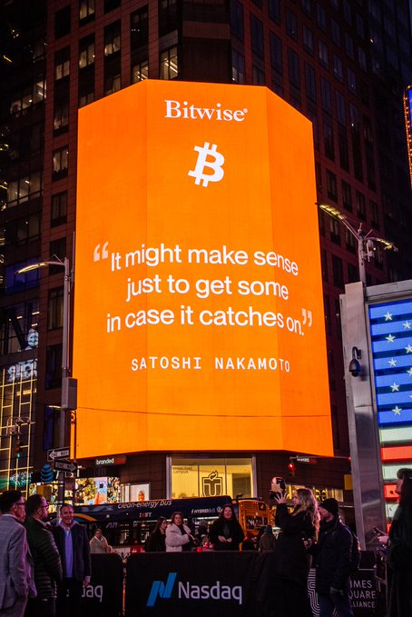 A large orange billboard in Times Square displays the Bitwise Bitcoin logo with a Satoshi Nakamoto quote: 'It might make sense just to get some in case it catches on.'