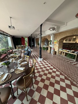 The interior of an elegant restaurant or hotel dining room with a checkered red-and-white tile floor, set dining tables, a stone fireplace, and wooden barrel decorations.