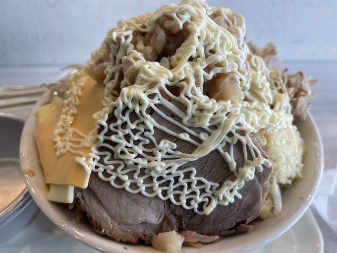 A Japanese dish featuring sliced beef and cheese covered with a generous drizzle of mayonnaise on rice in a white bowl.
