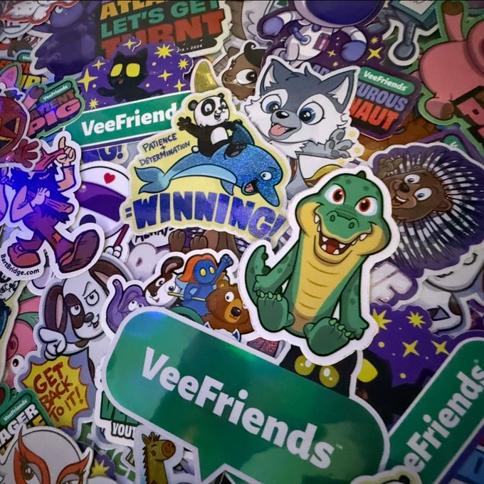 A pile of colorful 'VeeFriends' stickers featuring cartoon characters including an alligator, husky, panda, porcupine, and various motivational phrases like 'WINNING!', 'PATIENCE + DETERMINATION', and 'LET'S GET...'