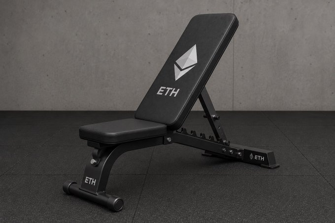 A black adjustable weight bench branded with the Ethereum (ETH) logo on the backrest and frame, set against a gray concrete wall in a gym setting.