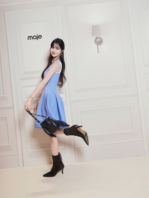 A person with long black hair is wearing a blue sleeveless dress and black high-heeled ankle boots, holding a black bag.