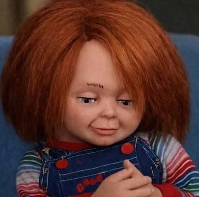 A close-up of the Chucky doll character from the horror films, featuring red hair, freckles, and a striped shirt with denim overalls, looking mischievous.