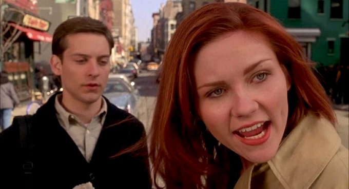 Peter Parker looks concerned while Mary Jane leans toward the camera with a distressed, almost tearful expression on a New York street, visually echoing the mix of worry and dramatic optimism behind the "he's not broke, Uptober is still loading" crypto rally meme.