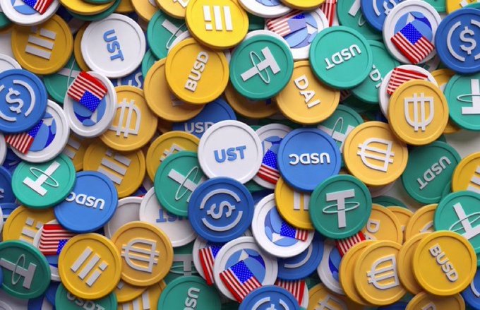 A colorful pile of round tokens labeled "UST" and "USDC," featuring dollar signs and the U.S. flag, represents the growing stablecoin market into which Open Standard's new Open USD stablecoin is entering, backed by major financial and crypto firms.
