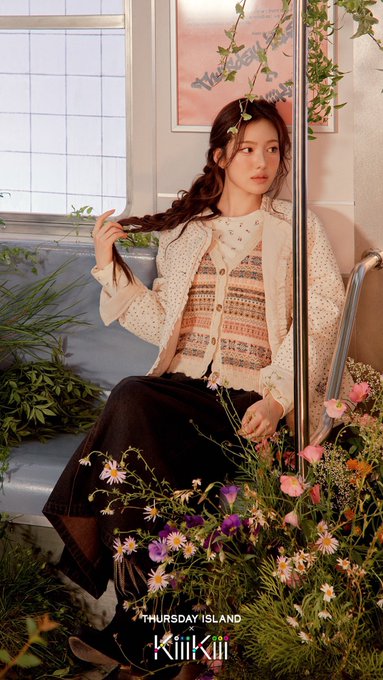 Sui poses among wildflowers and greenery on a blue bench for Thursday Island's 2026 Fall Campaign, wearing a cream knit cardigan and patterned vest, with the "THURSDAY ISLAND" and "KiiiKiii" text displayed at the bottom of the image.