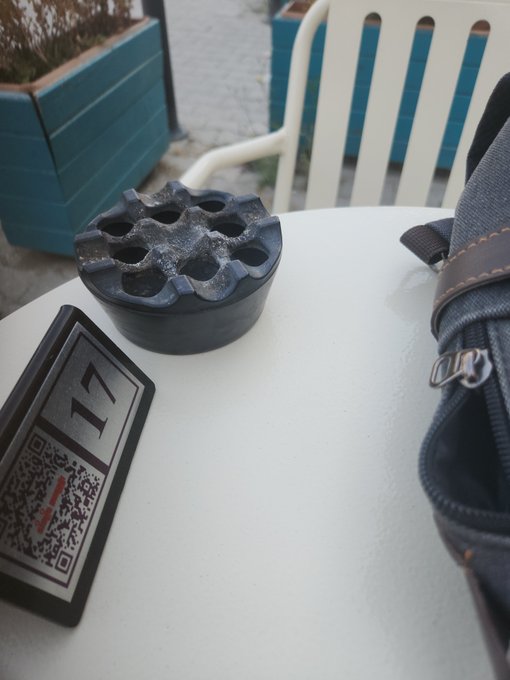 A black metal flower frog, a small framed sign with a QR code, and a bag sit on a white patio table.