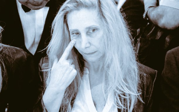 The image features an older woman with blonde hair, dressed in a suit or tuxedo, making a peace sign gesture by placing her index finger over her eye. The photo has been edited to include text that reads "I come to say that Karina Milei is formally charged in the case for the $Libra scam." This suggests that the image may be related to an investigation into the case of Karina Milei, a woman who was involved in a financial fraud scheme.