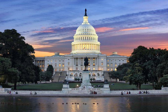 A photograph of the U.S. Capitol Building at sunset, viewed across a reflecting pool.