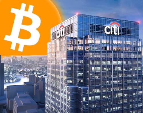 The image shows a Citigroup skyscraper with the Citi logo, set against a city skyline, paired with a Bitcoin logo—visually linking the bank's revised bearish outlook on Bitcoin's price target to the institution issuing the forecast.