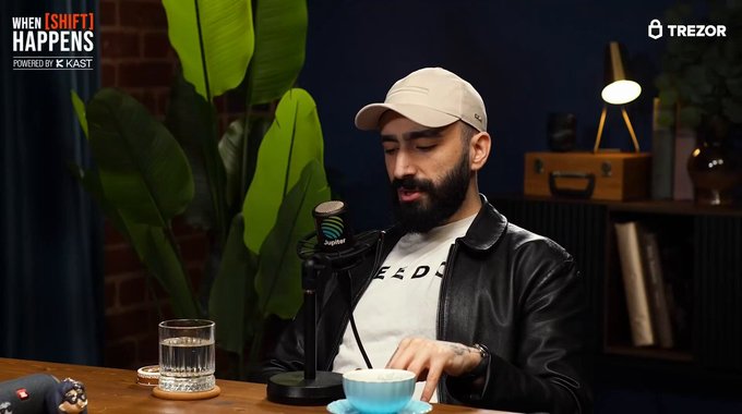 A bearded man in a white cap and black leather jacket sits at a podcast desk with a "When (Shift) Happens Powered by K-Kast" logo in the corner and a Trezor logo visible, speaking into a microphone. The caption reflects a discussion about Solana being the global Silicon Valley of crypto, emphasizing its strong developer ecosystem.