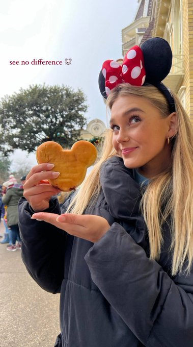 A blonde woman wearing Minnie Mouse ears holds up a Mickey Mouse-shaped waffle with the text "see no difference 🐭" overlaid, smiling at the camera at what appears to be a Disney park. The caption adds a cheerful "gm guys..! Happy Friday" greeting, making it a playful, weekend-ready social media post celebrating the Disney experience.