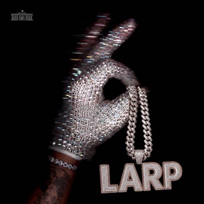 A diamond-encrusted glove holding a chain and a pendant spelling 'LARP' against a black background, with a small White House logo in the upper left corner.