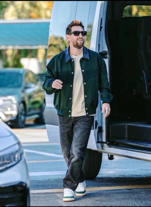 A bearded man wearing sunglasses, a dark green jacket, and jeans walks out of a vehicle in a parking lot.