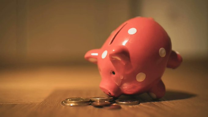 A pink piggy bank with white polka dots sitting on a wooden surface next to a few scattered coins in warm lighting.