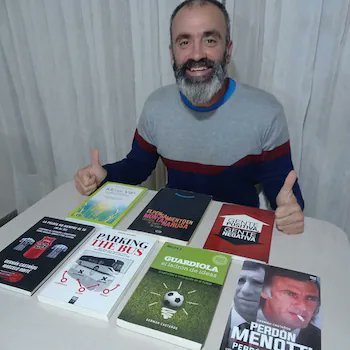 A bearded man wearing a striped sweater sits at a table giving two thumbs up, displaying a collection of sports books including 'Pardiens de la Furia', 'Guardiola', 'Perdón Menotti', and 'Pensar el Fútbol'.