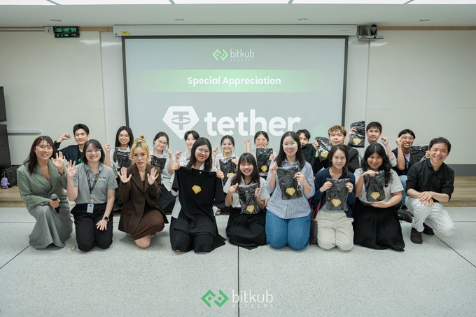 A group photo of people posing at a Bitkub Online event with a 'tether Special Appreciation' screen behind them, holding branded merchandise.