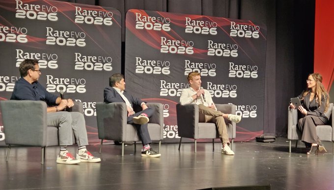 Four panelists sit on stage at Rare Evo 2026 against a backdrop displaying the event's logo, engaged in a discussion on stage. From left to right are Cisco Aguilar, Ron Hammond, John Medel, and Elizabeth Ha, discussing modernization, innovation, and transparency in government.