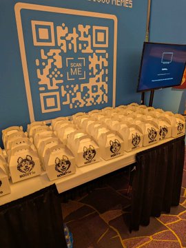 A conference booth setup features a large QR code banner reading 'SCAN ME' above a table lined with numerous white paper bags, each printed with a wolf-like logo and 'NEXUS AI' text.