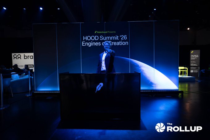 A man in a suit stands on stage pointing forward at the Robinhood HOOD Summit '26 'Engines of Creation' event, with 'The ROLLUP' logo in the corner.