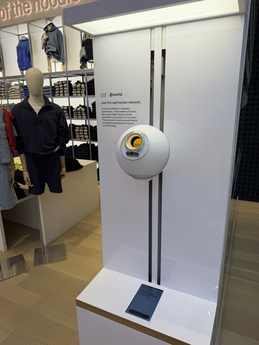The image shows a display of a white object, possibly a clock or a coin, mounted on a wall inside a store. The object is surrounded by clothing items such as shirts and jackets, which are hanging from racks nearby. A mannequin dressed in black attire can be seen among the clothing items. The post about Scam Altman's world coin trick seems to be related to this display, possibly suggesting that the coin was used as a part of a scheme or a prank involving fake coins.

The image does not provide enough information to determine if the coin is genuine or fake. However, it appears that the store has incorporated the coin into their display in some way, either for sale or as an interesting decoration.