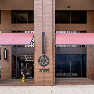 The image shows the exterior entrance of a building marked "CFTC" with a circular emblem, representing the U.S. Commodity Futures Trading Commission—the regulatory body referenced in the post for issuing Staff Letter 26-25 extending phantom no-action relief to passive software providers.