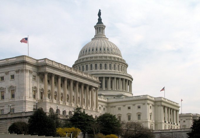 A daytime photograph of the United States Capitol building with American flags flying on top.