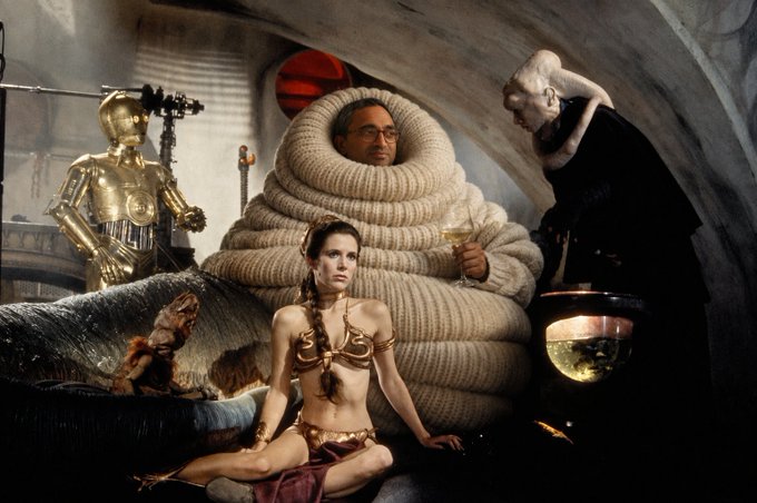 A scene from a Star Wars film shows characters including C-3PO, Bib Fortuna, Leia in her gold bikini outfit, and Jabba the Hutt inside his palace.