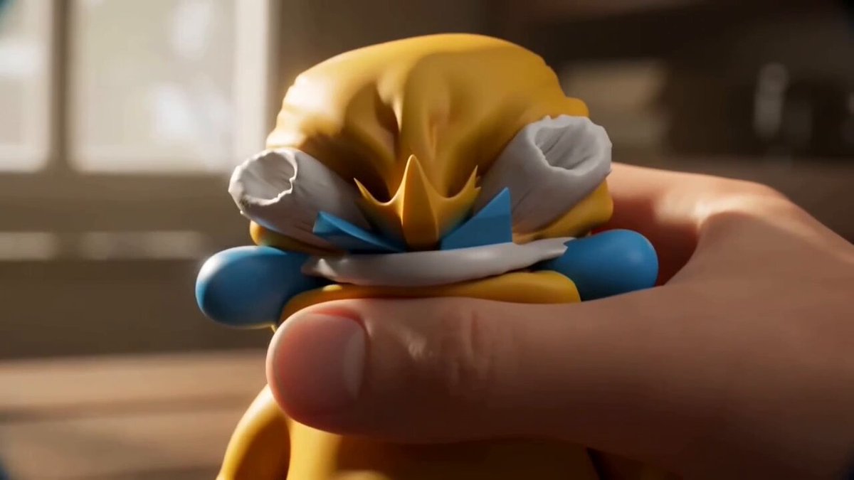 The image features a small yellow toy figurine with blue accents, held up by someone's hand. The figurine appears to be made of clay or plastic, giving it a unique texture. The person holding the figurine has a big smile on their face, which adds a sense of joy and positivity to the scene. The image also contains text that reads "JACK DUVAL FOR THE LOVE OF GOD JOIN THE GOOD SIDE AND APE" and "IMAGINE CRYING IN LAUGHTER SHEDDING A FEW CALORIES FROM THAT FATASS." This suggests a lighthearted, fun atmosphere related to the figurine.