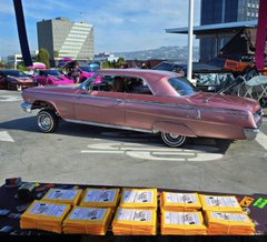 A pink classic car is parked on a street in Temecula, California, with stacks of yellow-wrapped prescription bottles labeled "PULSECHAIN" displayed on the pavement in front of it, promoting an RSG Foundation volunteer event to help distribute medication labels to over 1 million homes.