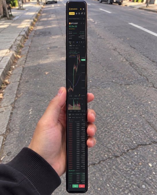 A hand holds a smartphone displaying the Binance trading app, showing Bitcoin (BTC/USDT) priced at $55,354.50 with candlestick charts and trade data visible against a backdrop of a street, suggesting a mobile crypto check-in on the go.