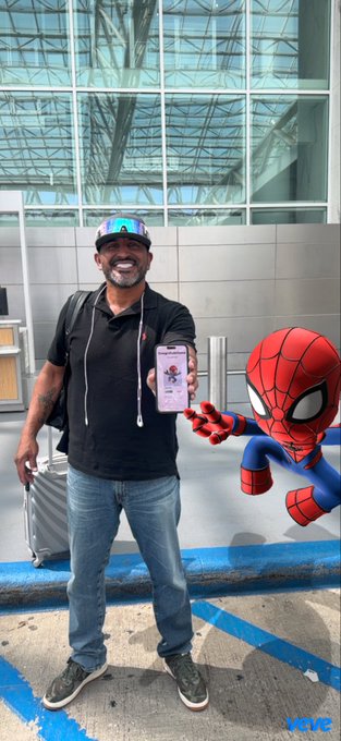 A man posing for a photo outside a convention center with an edited Spider-Man character holding his phone.