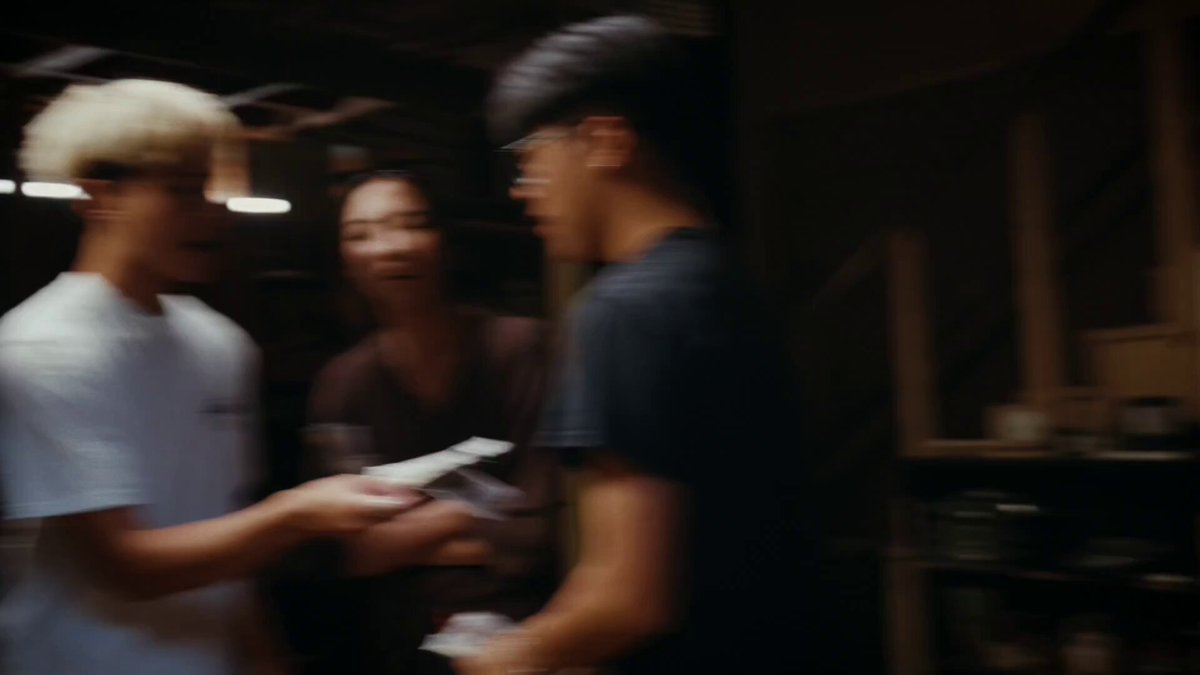 The image shows a group of people standing together in a room with a gray background. One person is holding a gun, while another person is handing over a piece of paper or a small object. The third person appears to be engaged in conversation with the first person who is holding the gun. The overall atmosphere seems to be casual and friendly as they interact with each other.
